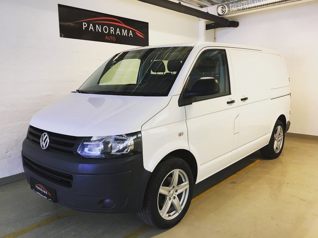Hvit Volkswagen Transporter inne i lokalet, med Panorama Auto skilt på veggen